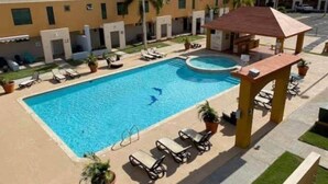 Una piscina con sillones de descanso y un pabellón, rodeada de edificios con balcones.