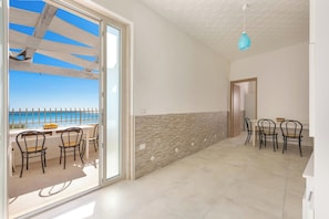 Habitació amb vistes al mar, zona de menjador amb cadires, taula i una làmpada penjant blava.