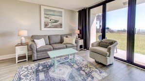 Un salon avec un canapé, un fauteuil, une table basse et un tableau accroché au mur.