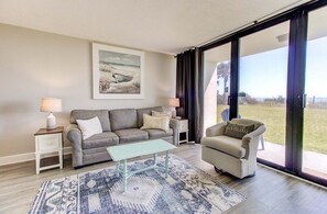Un salon avec un canapé, un fauteuil, une table basse et un tableau accroché au mur.
