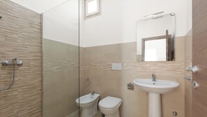 Ein modernes Badezimmer mit einer Duschkabine aus Glas, einem weißen Waschbecken und zwei Toiletten.