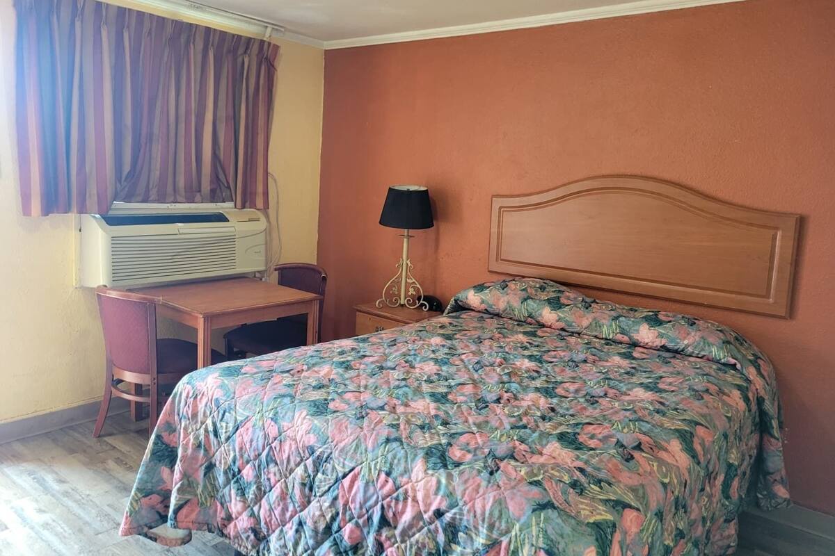Una habitación de hotel con una cama, un escritorio, una lámpara y un equipo de aire acondicionado.