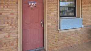 A red door with the number 102, a window with an air conditioning unit, and a welcome mat. - Relax Inn Daingerfield Near Mount Pleasant TX (Daingerfield)