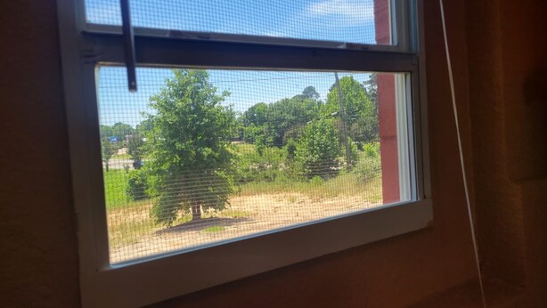 A window with a view of a green landscape, including trees and a fence. - Relax Inn Daingerfield Near Mount Pleasant TX (Daingerfield)