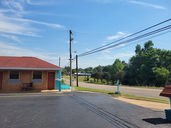 A building with a red roof and a number '101' on the door, a parking lot, and a road with trees and power lines in the background.