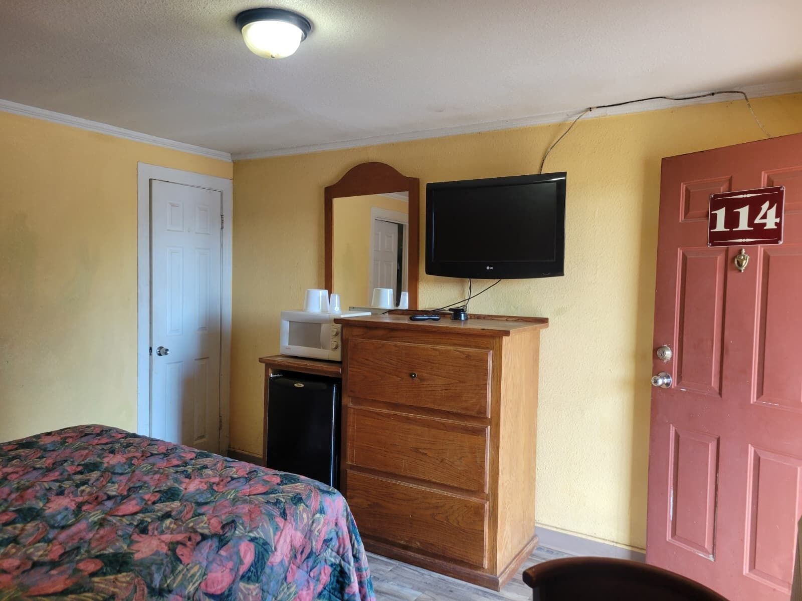 A bedroom with a bed, dresser, television, microwave, and a door with the number 114.