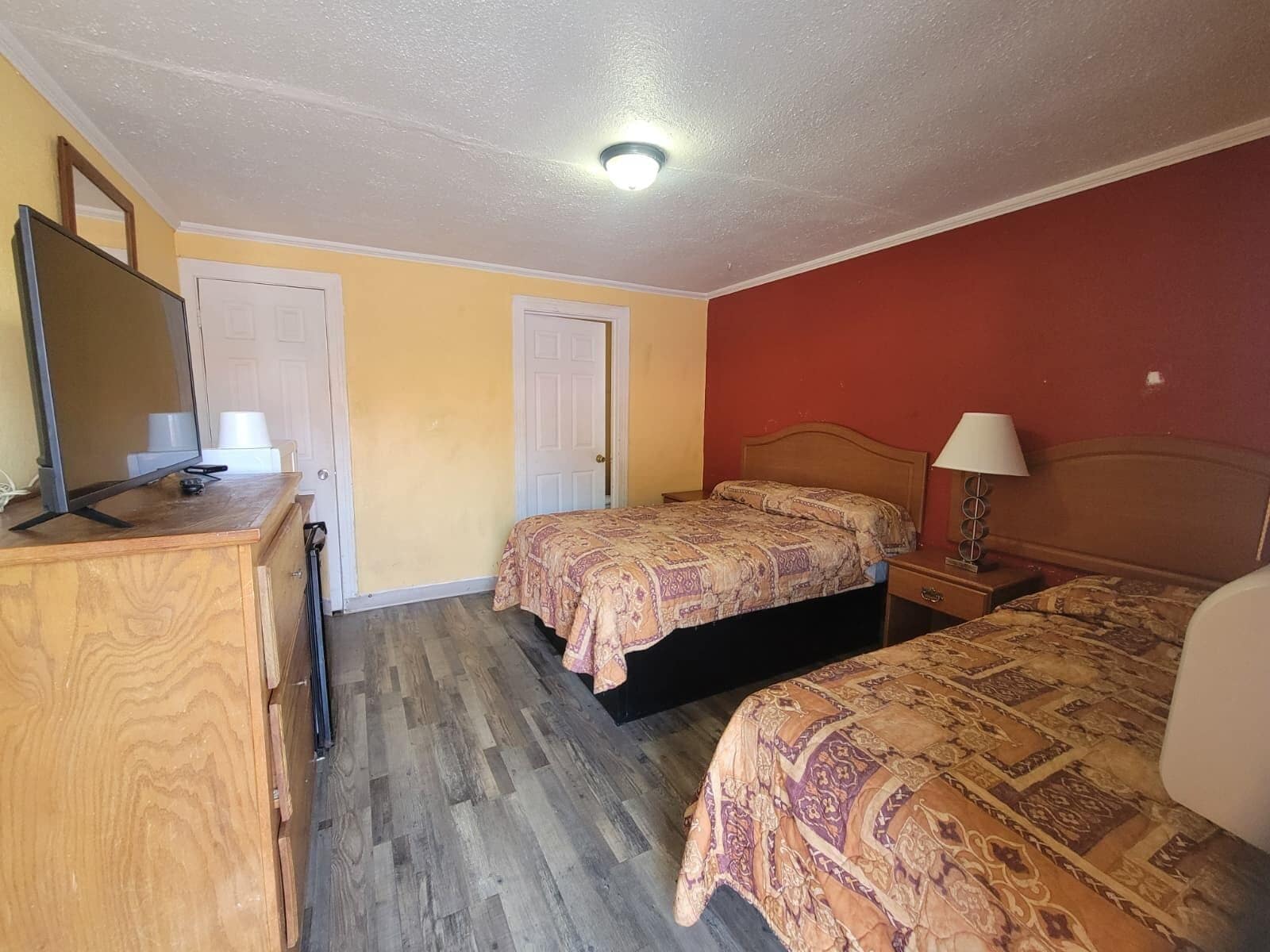 Une chambre avec deux lits, une commode, un miroir et un luminaire au plafond.