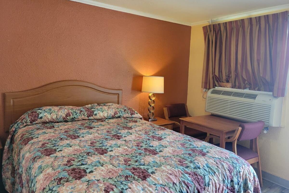 Una habitación de hotel con una cama, un escritorio, una silla, aire acondicionado y cortinas.