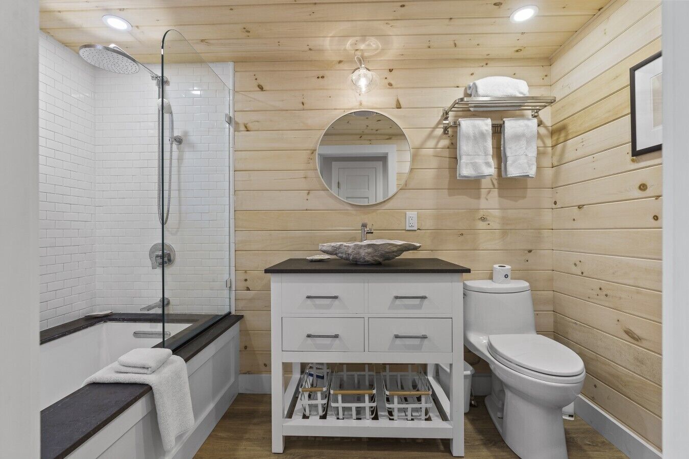 A compact bathroom with a shower, toilet, and sink, featuring wooden walls and a mirror.