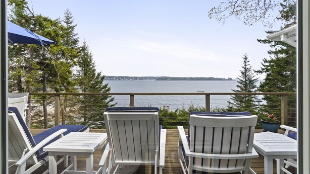 A deck with white chairs and a table, overlooking a body of water and trees. - Oceanfront Retreat on Spruce Point, Private Dock, Hot Tub & Resort Amenities (Boothbay Harbor)