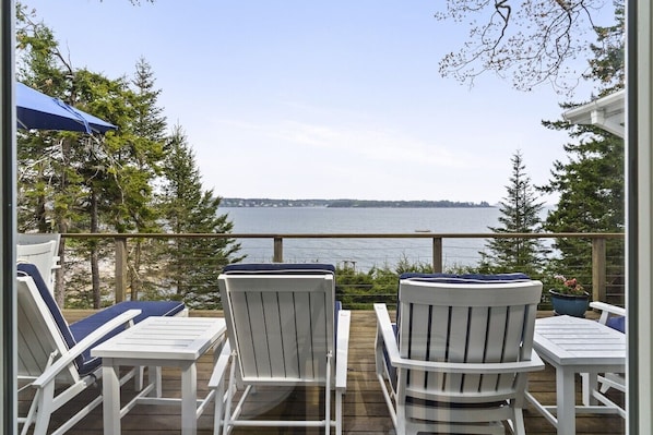 A deck with white chairs and a table, overlooking a body of water and trees. - Oceanfront Retreat on Spruce Point, Private Dock, Hot Tub & Resort Amenities (Boothbay Harbor)
