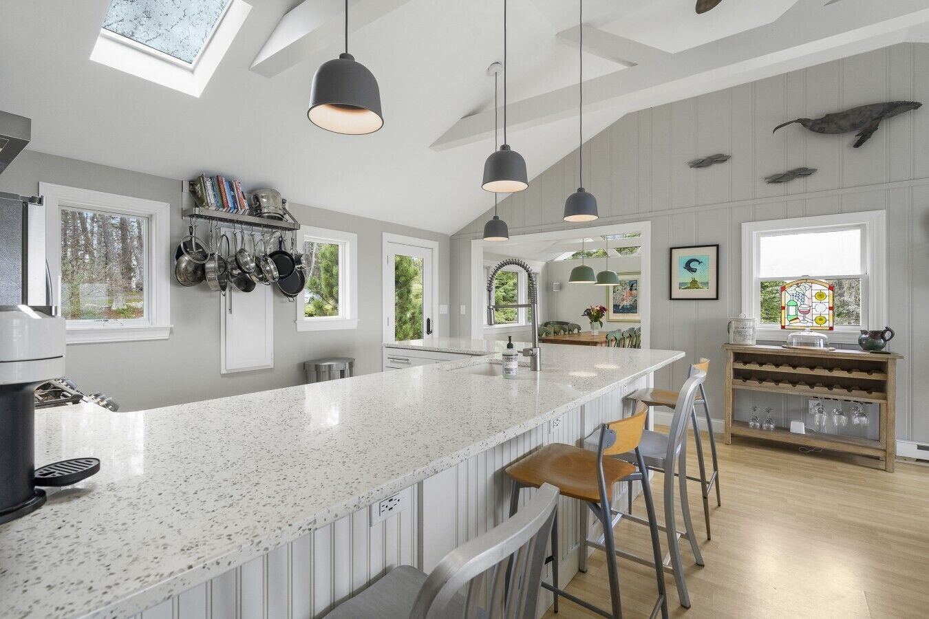 Une cuisine moderne dotée d’un grand îlot central, de luminaires suspendus et offrant une vue sur l’extérieur.