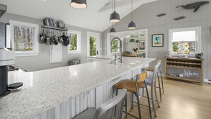 A modern kitchen with a large island, pendant lights, and a view of the outdoors. - Oceanfront Retreat on Spruce Point, Private Dock, Hot Tub & Resort Amenities (Boothbay Harbor)