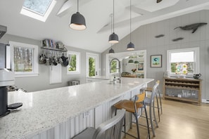 A modern kitchen with a large island, pendant lights, and a view of the outdoors. - Oceanfront Retreat on Spruce Point, Private Dock, Hot Tub & Resort Amenities (Boothbay Harbor)