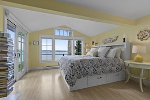 A bedroom with a bed, a bedside table, a lamp, a window with a view, and a stack of books. - Oceanfront Retreat on Spruce Point, Private Dock, Hot Tub & Resort Amenities (Boothbay Harbor)