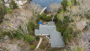 A house with a sloped roof, a deck, and a small outdoor seating area. - Oceanfront Retreat on Spruce Point, Private Dock, Hot Tub & Resort Amenities (Boothbay Harbor)