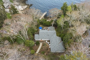 A house with a sloped roof, a deck, and a small outdoor seating area. - Oceanfront Retreat on Spruce Point, Private Dock, Hot Tub & Resort Amenities (Boothbay Harbor)