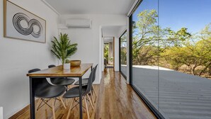 Ein modernes Interieur mit einem Holztisch, schwarzen Stühlen, einer Topfpflanze und einem großen Fenster mit Blick auf Bäume.
