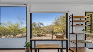 Ein Zimmer mit einem großen Fenster, einem Holztisch, einer Bank und einem Metallregal.