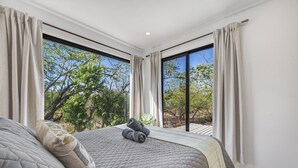 Ein Schlafzimmer mit einem großen Bett, zwei Fenstern und Blick auf Bäume.
