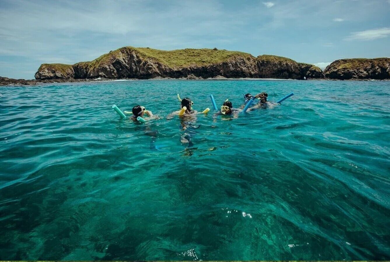 Un groupe de personnes fait de la plongée avec tuba dans une eau d’un bleu cristallin, avec des formations rocheuses en arrière-plan.