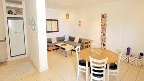 Een compacte leefruimte met een kitchenette, een bank, een eettafel met stoelen en een kleurrijk gordijn.