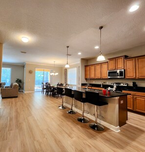 A spacious kitchen with wooden cabinets, a stainless steel microwave, and a dining area with a long table and chairs. - Spacious 6BR Family Villa, 13 miles to Disney, Private Pool, Resort Waterpark (Kissimmee)