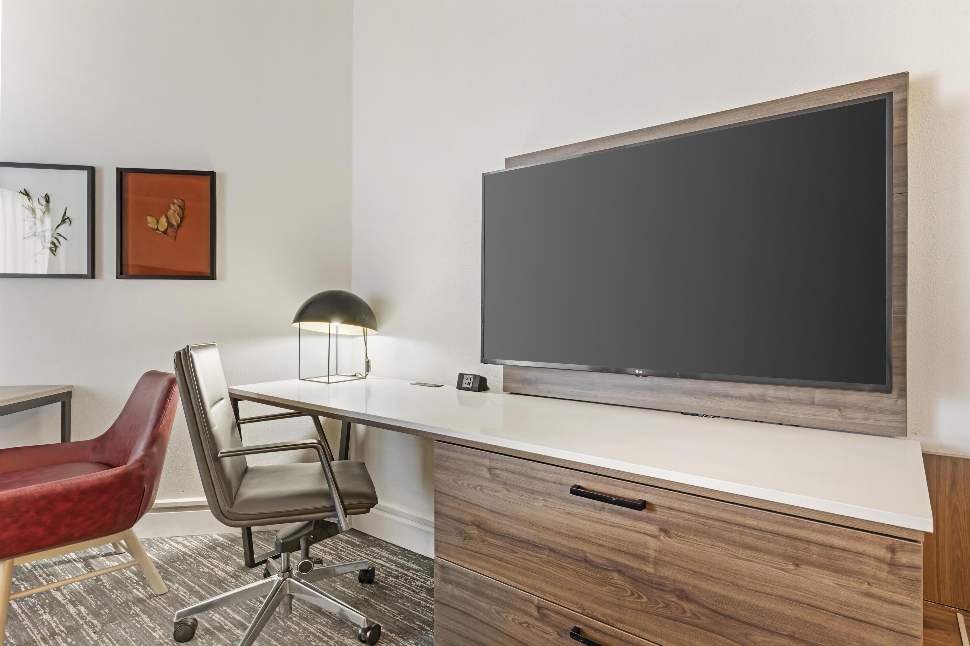 A modern office space with a white desk, a red chair, a large blackboard, and two framed pictures on the wall.