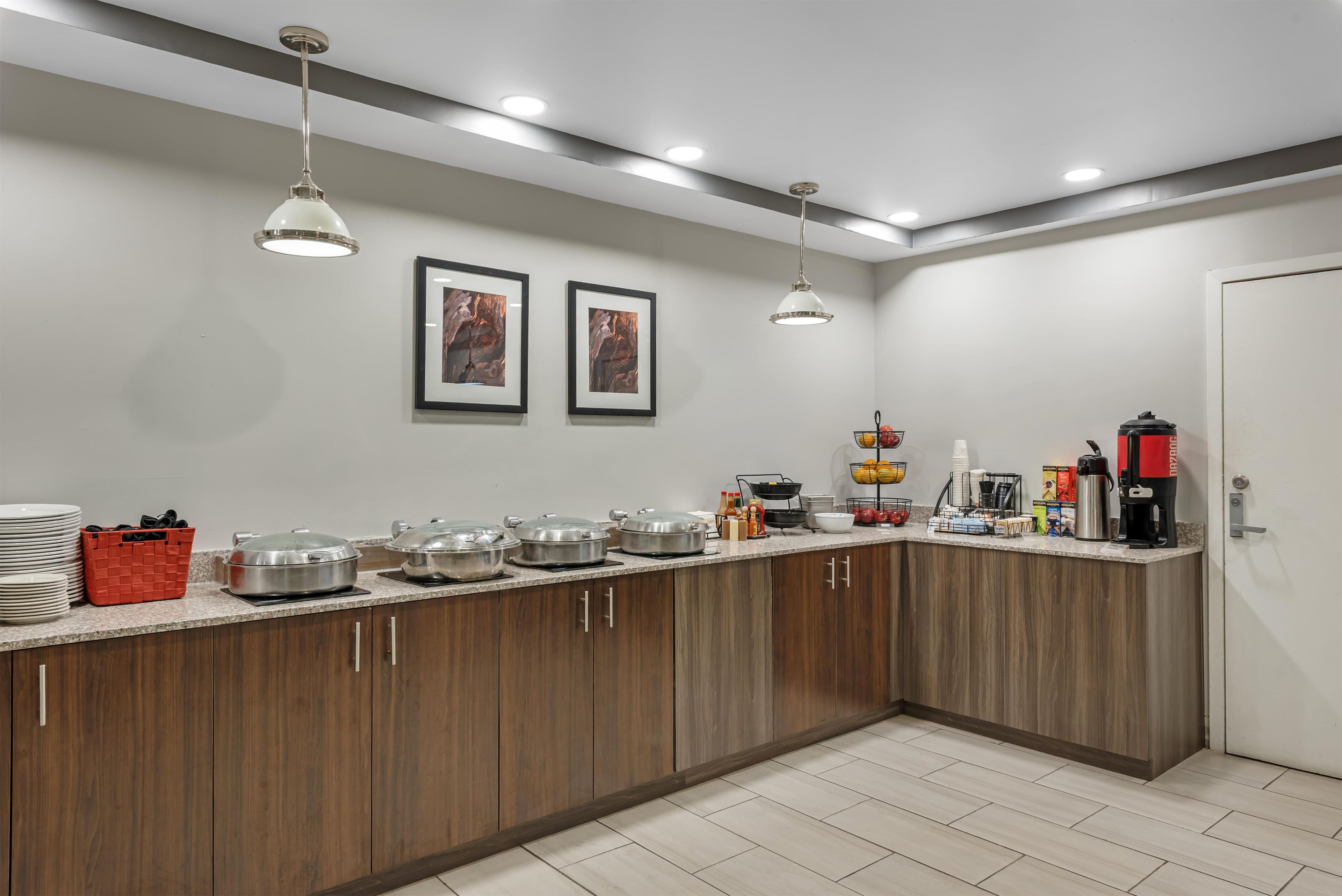 A kitchen with wooden cabinets, a countertop with various appliances, and two framed pictures on the wall.