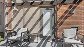 A patio with two chairs, a small round table, and a glass door leading to a brick building.
