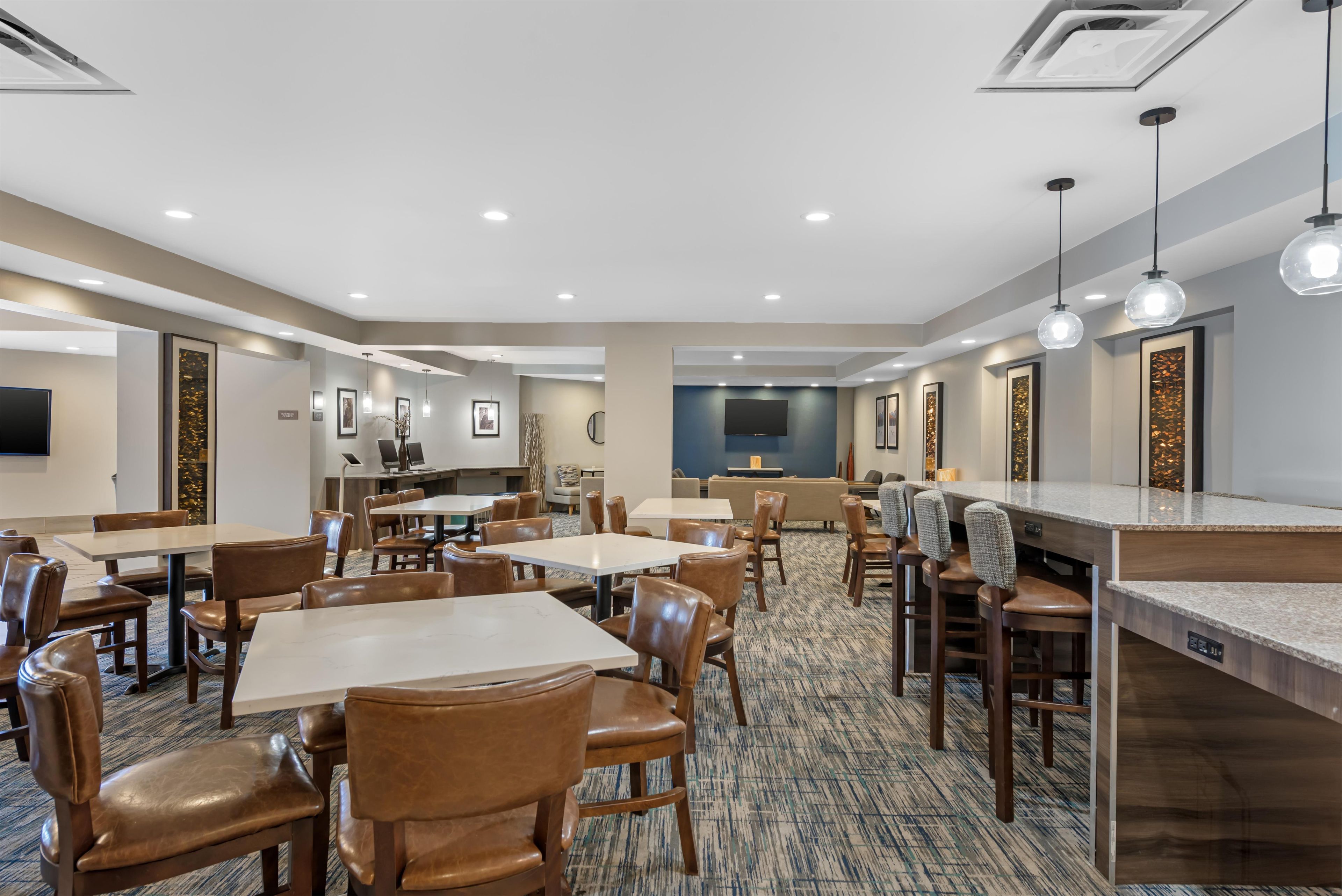 A hotel dining area with multiple tables and chairs, a bar area, and a television screen.