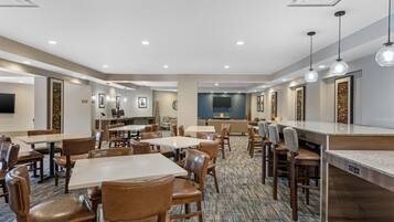 A hotel dining area with multiple tables and chairs, a bar area, and a television screen.