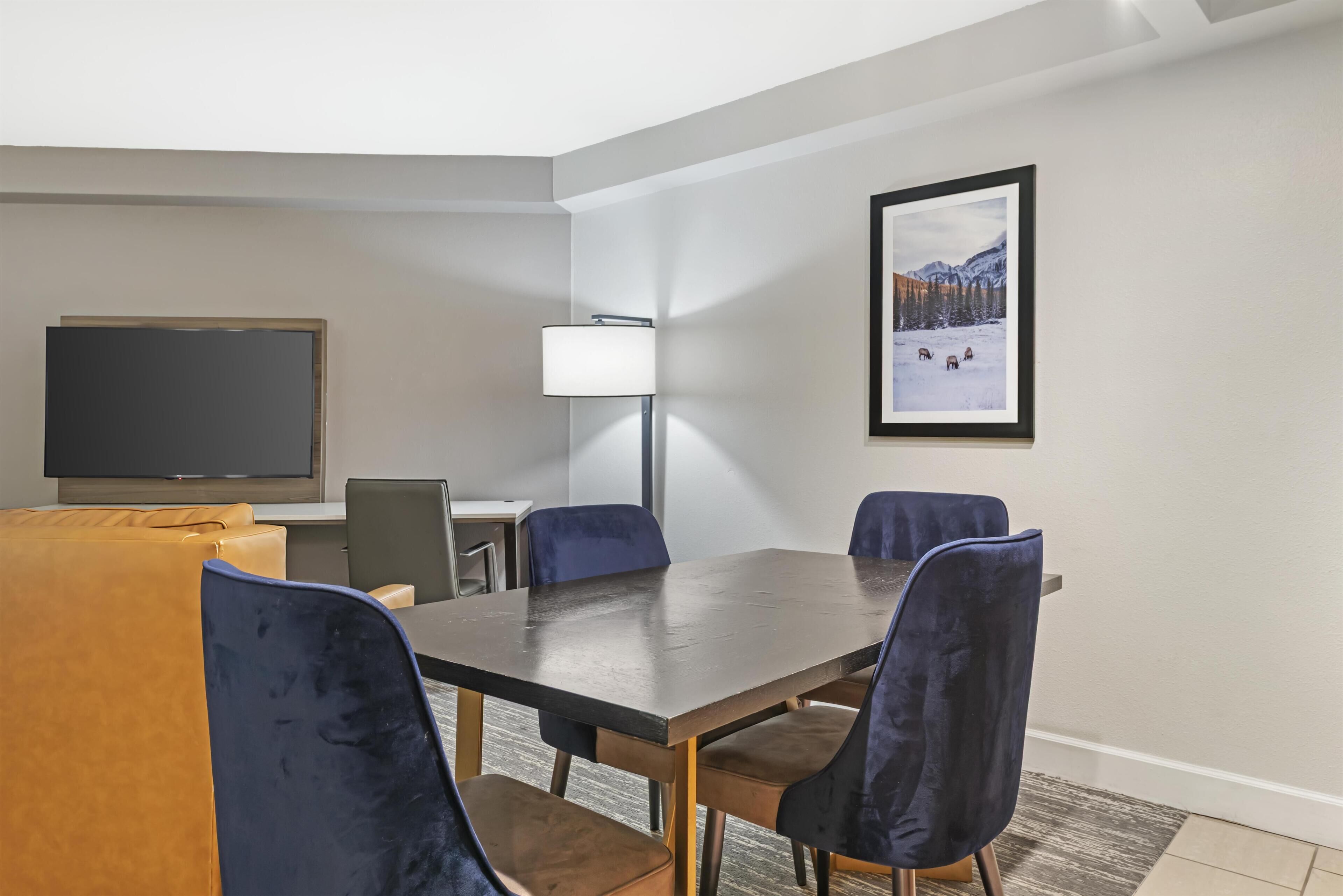 A conference room with a large table, four chairs, a television, and a lamp.