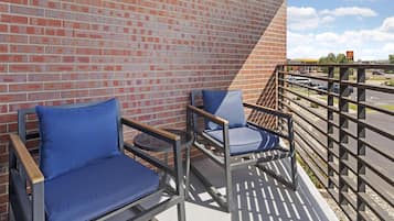 A balcony with two blue cushioned chairs, a brick wall, and a view of a parking lot with a McDonald's sign.