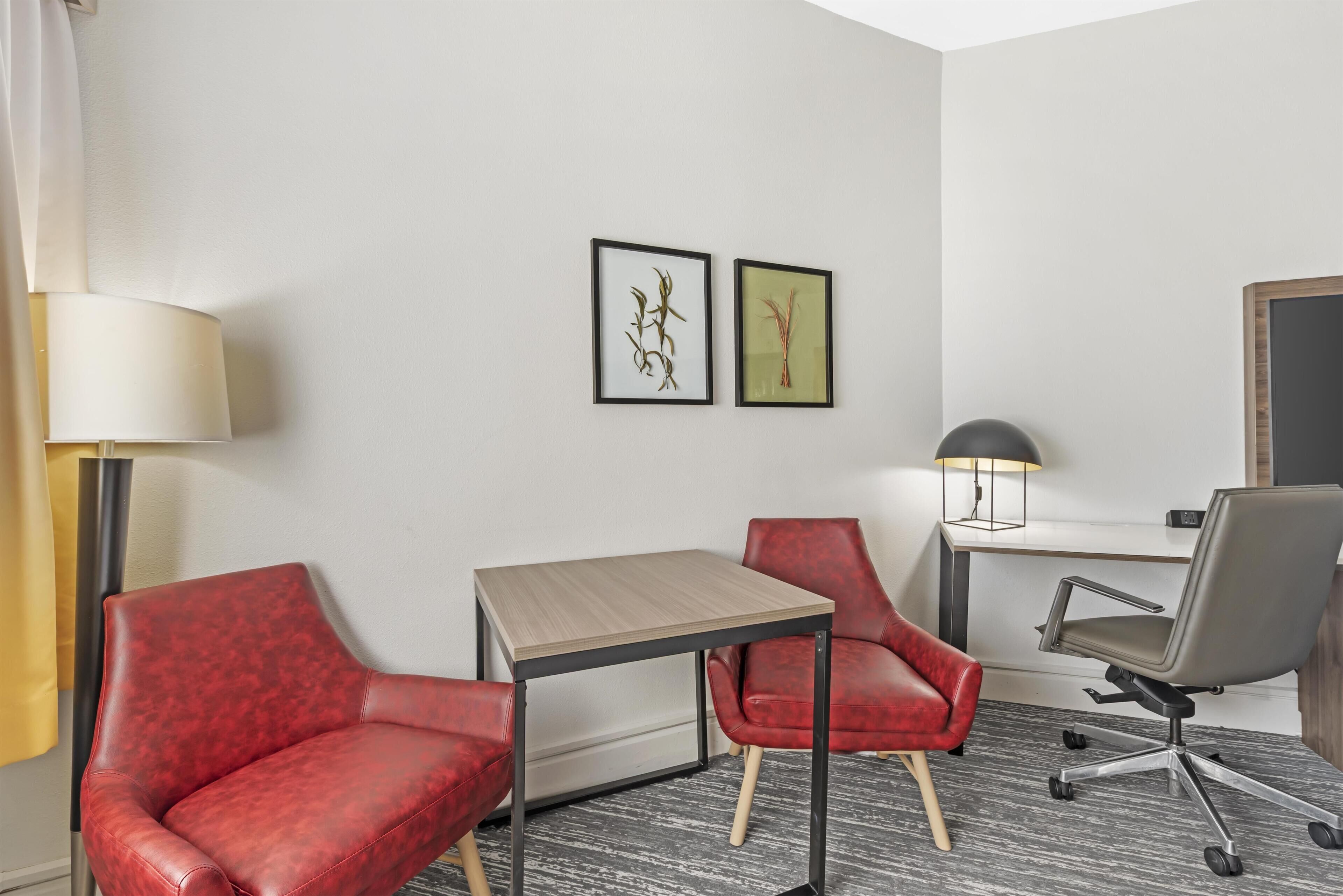 Ein Hotelzimmer mit Schreibtisch, zwei roten Sesseln, einer Lampe und zwei gerahmten Bildern an der Wand.