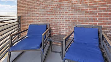 Un balcón con dos sillones de descanso y una pequeña mesa, un muro de ladrillo y una barandilla metálica.