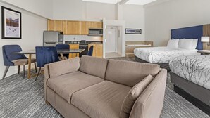 Habitación de hotel con sofá, cama, escritorio con silla, microondas y refrigerador.