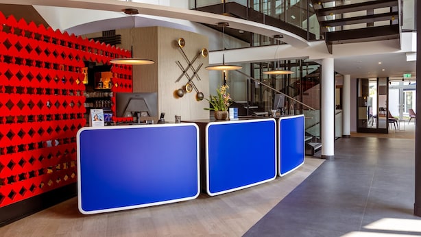 Ein Empfangsbereich im modernen Stil, mit einem blauen Empfangstresen, einer roten, geometrischen Wand und einer Treppe im Hintergrund.