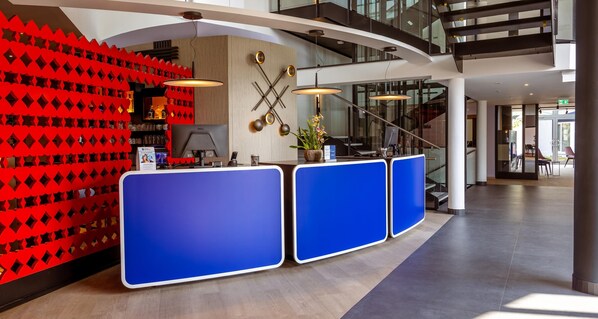 A reception area with a modern design, featuring a blue reception desk, a red geometric wall, and a staircase in the background. - Best Western Hotel Altenburger Land (Altenburg)