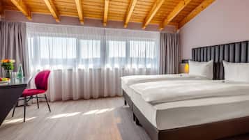 A hotel room with a wooden ceiling, a bed, a desk with a chair, and a window with curtains.
