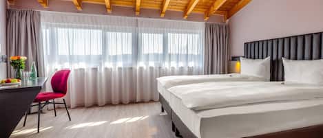 A hotel room with a wooden ceiling, a bed, a desk with a chair, and a window with curtains.