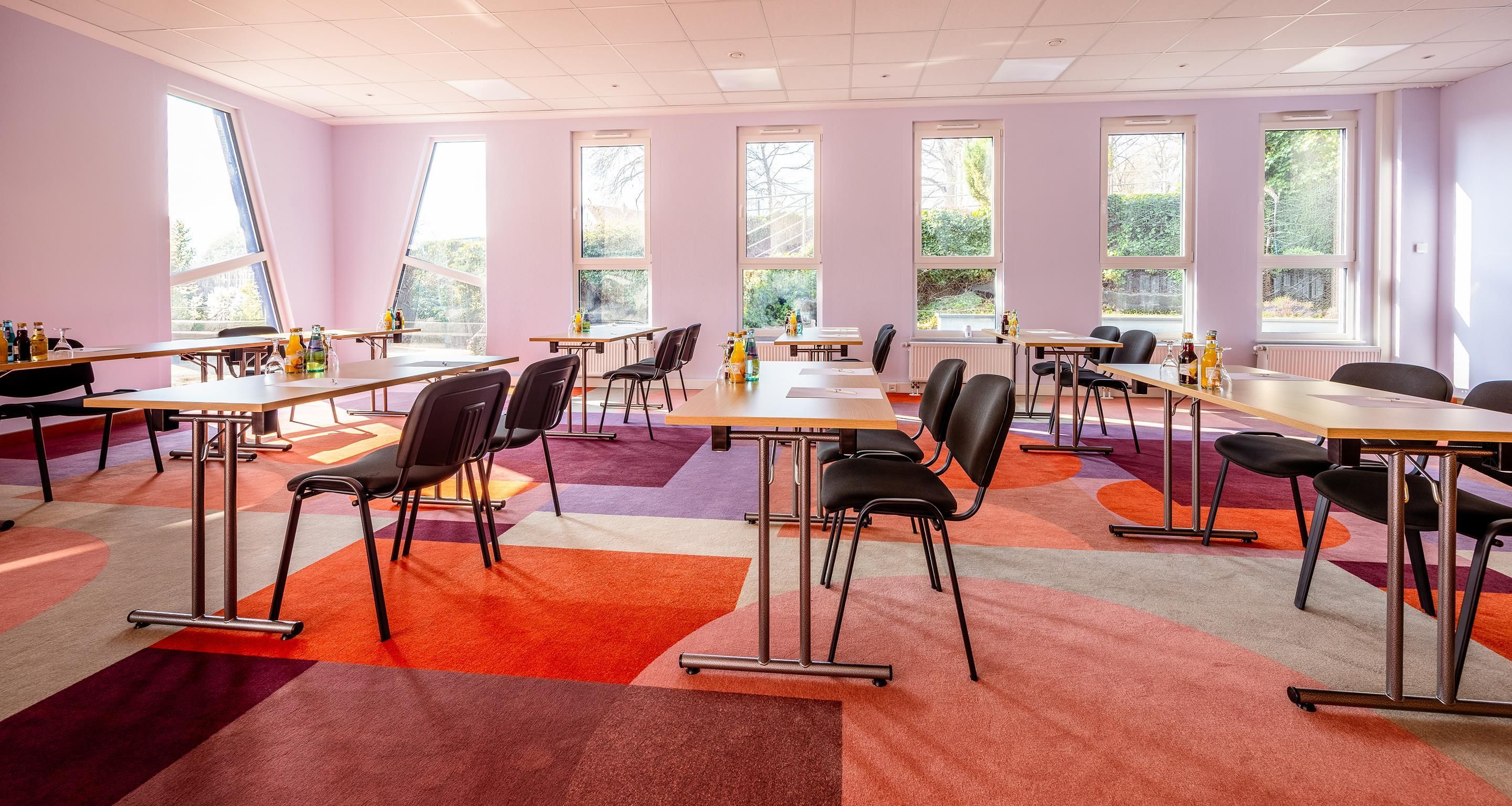 A conference room with multiple tables and chairs, large windows, and a colorful carpet.