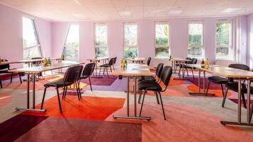 A conference room with multiple tables and chairs, large windows, and a colorful carpet.
