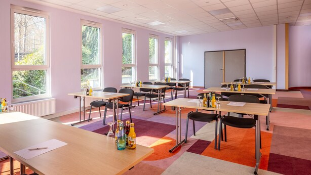 Une salle de conférence équipée de plusieurs tables, de chaises et d’un tableau blanc.
