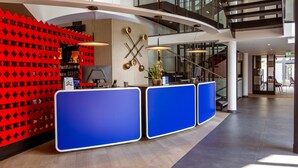 A modern reception area with a blue counter, red geometric wall, and a staircase in the background. - Best Western Hotel Altenburger Land (Altenburg)