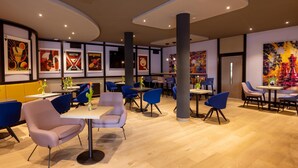 Interior moderno de restaurante con sillas azul y rosa, mesas de madera y diversas obras de arte en las paredes.