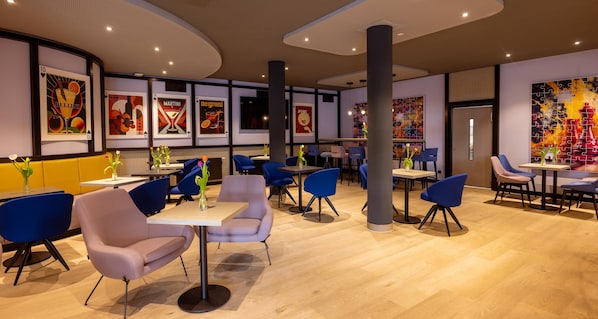 A modern restaurant interior with blue and pink chairs, wooden tables, and a variety of wall art. - Best Western Hotel Altenburger Land (Altenburg)