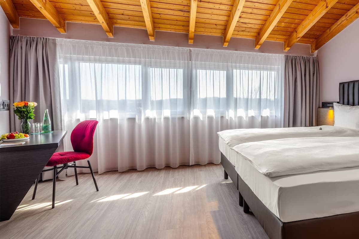 A bedroom with a bed, a desk, a chair, and a window with curtains.