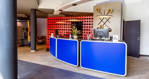 A reception area with a modern design, featuring a blue reception desk, a red patterned wall, and a unique ceiling light fixture. - Best Western Hotel Altenburger Land (Altenburg)