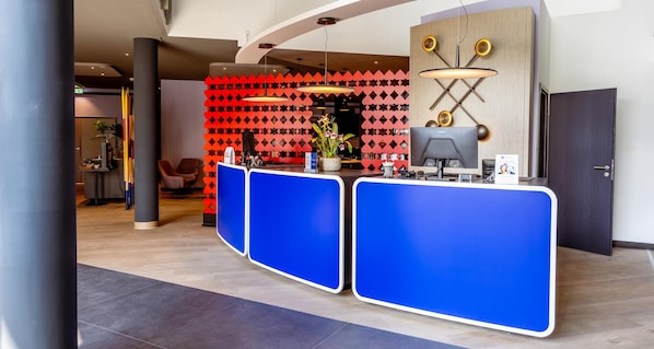 A reception area with a modern design, featuring a blue reception desk, a red patterned wall, and a unique ceiling light fixture. - Best Western Hotel Altenburger Land (Altenburg)